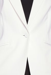 Vitt blazer med en enda rund knapp, slagkrage och två framfickor, tillverkat av slät tyg med en strukturerad passform.