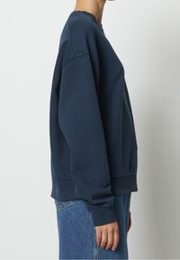 Sudadera azul marino con cuello redondo, mangas largas, puños y dobladillo acanalados. Presenta un ajuste relajado y una tela suave y texturizada.