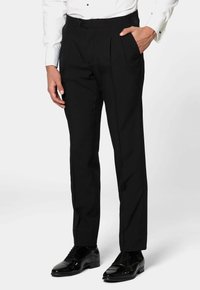 Pantaloni neri su misura con pieghe, caratterizzati da una texture liscia e tasche laterali, abbinati a eleganti scarpe lucide nere.