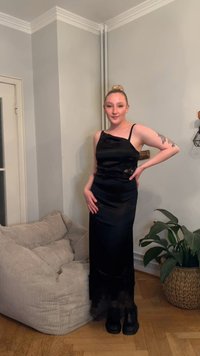 Fekete szatén ruha aszimmetrikus nyakkivágással és spagettipántokkal, testhez simuló sziluettel és oldalán finom virágos hímzéssel.