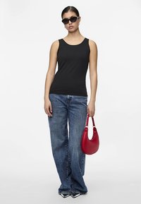 Juodas rankovių palaidinė, laisvos mėlynos kelnės, rankoje laikoma maža išlenkta raudona rankinė, dėvi tamsius akinius nuo saulės, lygi medžiaga, laisvo stiliaus.