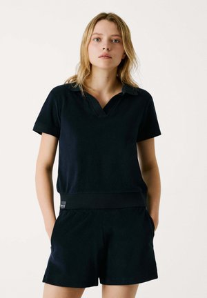 Navy cotton polo paita V-kauluksella, lyhyillä hihoilla ja ribatulla helmalla, yhdistettynä matchaaviin lyhyisiin shortseihin, joissa on sivutaskut ja joustava vyötärö.