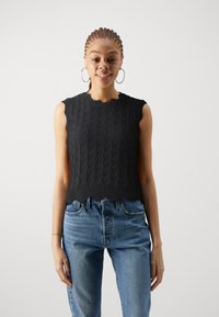 Haut sans manches en tricot noir avec un motif en vagues et un ourlet festonné, associé à un jean en denim taille haute bleu clair. Design et texture simples.