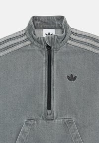 Felpa grigia con zip a quarti e colletto alto, tre strisce decorative sulle spalle e un piccolo logo nero sul petto. Texture morbida.