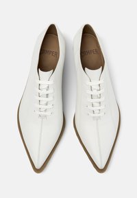 Λευκά δερμάτινα παπούτσια με μυτερή μύτη, εξοπλισμένα με έξι ζευγάρια λευκά κορδόνια και ελαφριά καφέ λαστιχένια σόλα. Διακριτό εσωτερικό λογότυπο.