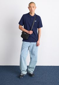 Námornícky modré polo tričko, svetlomodré voľné džínsy, čierne tenisky a malá čierna kabelka cez telo. Neformálny, moderný outfit s jednoduchým dizajnom.