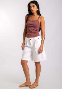 Top sin mangas color malva con tirantes finos que presenta tachuelas decorativas; combinado con pantalones cortos blancos hasta la rodilla y sandalias doradas con cordones. Tejido suave, corte relajado.