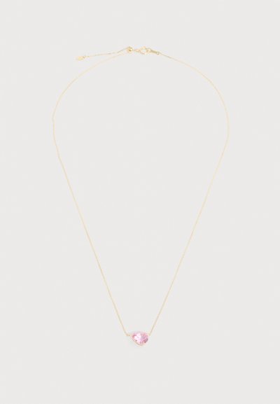 Λεπτή χρυσή αλυσίδα με μικρό, καρδιοειδές ροζ πέτρωμα ως μενταγιόν στο κέντρο πάνω σε ανοιχτό φόντο.
