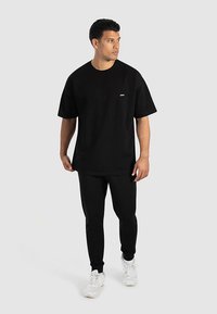 Svart bomulls-t-shirt med korta ärmar, avslappnad passform och liten logga på bröstet, kombinerad med matchande svarta joggers och vita sneakers.