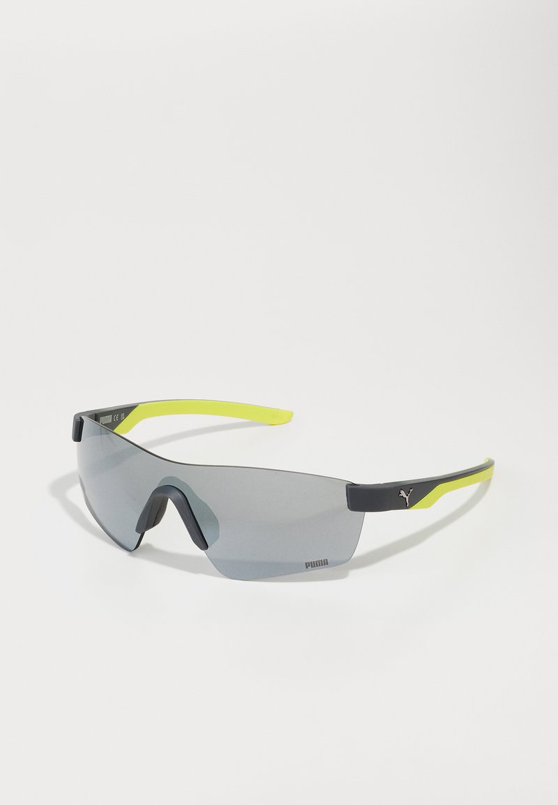 Lunettes de soleil Puma avec un design enveloppant, verres teintés gris, monture noire et accents jaune vif sur les branches.