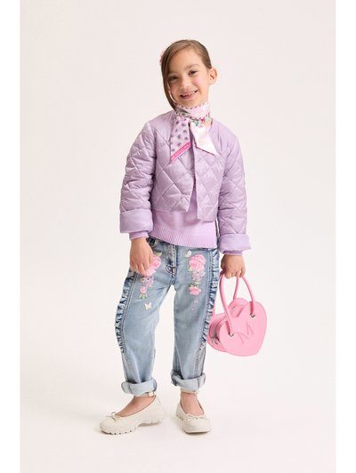 Νεαρή κοπέλα που φοράει μια λιλά καπιτονέ ζακέτα, τζιν με κεντήματα λουλουδιών, ένα κασκόλ με σχέδια στο λαιμό και κρατάει μια ροζ τσάντα χειρός σε σχήμα καρδιάς.