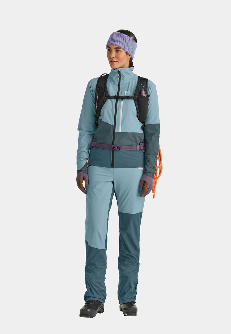 Technical outdoor outfit in shades of blue, featuring a zippered jacket, pants with textured accents, and a purple headband. Includes backpack and gloves.