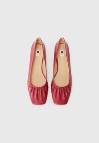 Ballerines en cuir rouge avec un bout carré, des détails froncés à l'avant et un intérieur lisse. Étiquette de taille visible à l'intérieur.