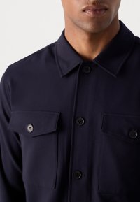 Chemise bleu marine à boutons, avec un col, deux poches poitrine avec rabat et une texture de tissu lisse.