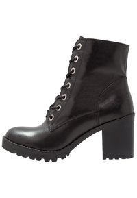 Bottines en cuir noir avec un talon épais, bout rond et un laçage à l'avant. Comprend des œillets argentés et une semelle texturée et à motifs.