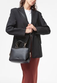 Sorte struktureret taske med en tekstureret overflade, dobbelt topstænger og en aftagelig skulderrem. Guldtonede hardwaredetaljer er synlige.