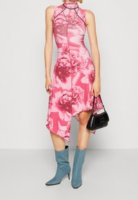Różowa sukienka w kwiaty z wysoką szyją, asymetrycznym dołem i teksturowanym materiałem. W parze z niebieskimi kozaczkami do kolan i czarną torebką.