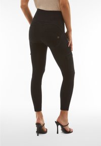 Leggings neri a vita alta con una texture simile al denim, dotati di tasche posteriori e una vestibilità sartoriale, accentuati da gambe sottili e una finitura pulita.