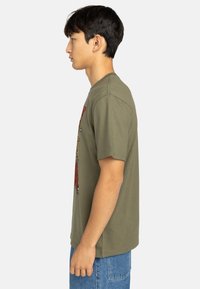 Olive green cotton T-shirt with short sleeves, featuring a multicolored graphic print on the front and a relaxed fit.