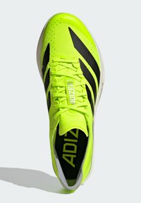 Neonkeltaiset urheilukengät mustilla yksityiskohdilla, verkkokuvioisella päällisellä ja näkyvällä logolla. Varustettu pyöreillä kengännauhoilla ja kuvioidulla pohjalla pitoa varten.