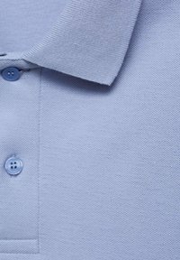 Vaaleansininen polo-paita, jossa on teksturoitu kangas, kauluksessa on kaulus, kaksi nappia ja siisti ommel yksityiskohtina.