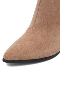 Béžové semišové členkové topánky s špicatou špičkou a štíhlym siluetou. Hladká textúra s čiernou gumovou podrážkou a minimálnymi švovými detailmi.