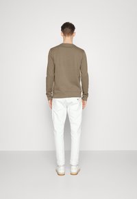 Sudadera de manga larga color verde oliva con puños y dobladillo acanalados, combinada con pantalones blancos ajustados y zapatillas blancas, vista desde atrás.