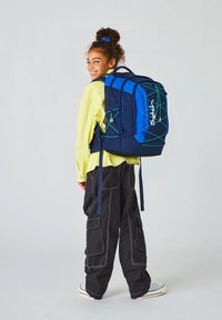 Blauer und marinefarbener Rucksack mit grünen Akzenten und einem Logo, ausgestattet mit einem gepolsterten Rücken, verstellbaren Trägern und sechs Taschen, getragen von einer Person.