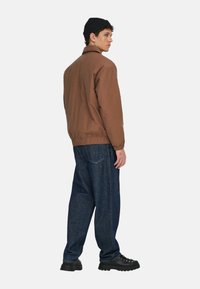 Braune Elastanjacke mit Kragen, gerippten Bündchen und elastischem Saum, kombiniert mit locker sitzenden dunklen Denim-Jeans und schwarzen Schnürstiefeln.