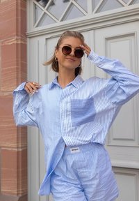 Vaaleansininen ja valkoinen raidoitettu ylipitkä napillinen paita, jossa on rintatasku, yhdistettynä samansävyisiin Shortseihin. Ominaisuuksina pehmeä materiaali ja rento leikkaus.