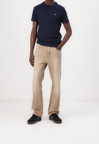 Camiseta azul marino con un pequeño logotipo, combinada con jeans de pierna recta beige claro y zapatillas negras con detalles blancos. Atuendo sencillo y casual.