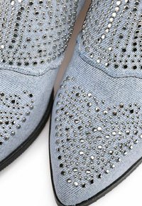 Stivaletti in denim con punta appuntita, decorati con borchie argentate a forma di cuore e una finitura testurizzata di un azzurro chiaro.