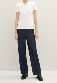 Vit kortärmad polo med knappslå, parat med mörkblå vida jeansbyxor och svarta snörskor.