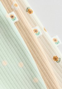 Sæt med tre ribbede stofpaneler i pastelfarver: mintgrøn med prikkermønster, fersken med blomsterdesign og cremefarvet med små blomster.