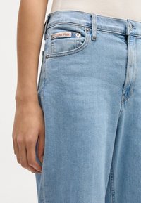 Šviesiai mėlynos džinsinės kelnės su tiesiu kirpimu. Ypatybės apima Calvin Klein logotipą ant kišenės, metalinius mygtukus ir penkių kišenių dizainą.