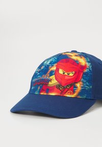 Kék baseball sapka élénk grafikai ábrázolással, amelyen egy ninja karakter látható, ívelt szélekkel és állítható hátsó pánttal.