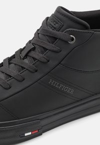 Czarne wysokie trampki z czarnymi sznurówkami, z wytłoczonym napisem "HILFIGER" na boku oraz małym czerwono-białoniebieskim logo na krawędzi podeszwy.