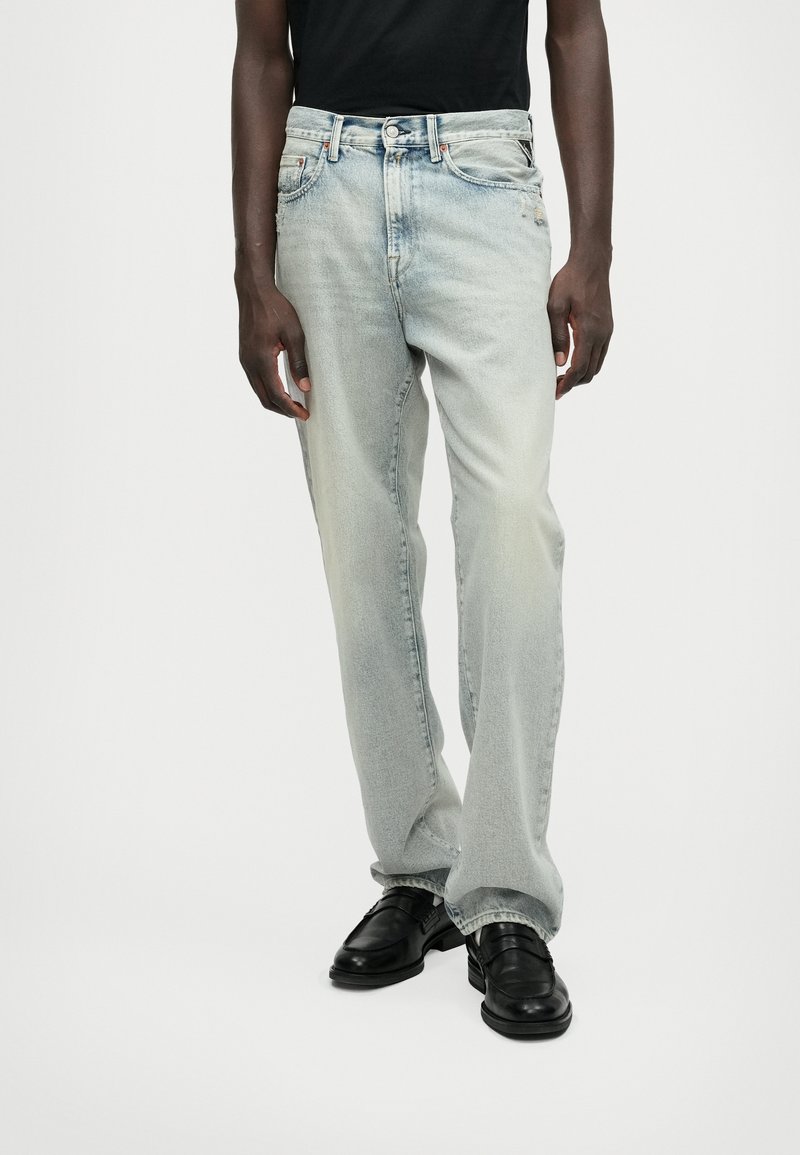 Jeans denim azul claro, ligeiramente desgastados, com um corte reto. Apresenta cinco bolsos, fecho de botão e um tom desbotado.