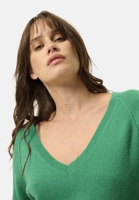 Pull vert en v en tricot doux, avec une coupe décontractée et une texture subtile, des manches longues et un col net.