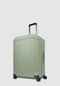 Maleta rígida en verde claro, con textura acanalada, asa retráctil, cuatro ruedas y asa lateral de transporte.