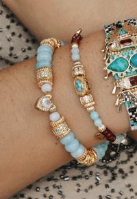 Trois bracelets avec des accents en or, des perles turquoises et aquamarines, des strass clairs et des designsintriqués sur une surface texturée.