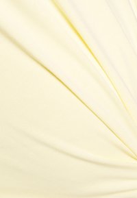 Tecido amarelo claro que apresenta uma textura suave com um leve brilho, apresentando dobras drapeadas e uma superfície lisa e uniforme.