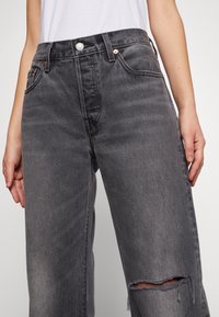 Grå höga jeans med en avslappnad passform, med ett rivet knä, kopparnitar och en texturerad denimfinish.