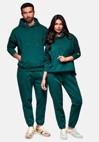Grön hoodiedräkt och sweatpants set gjort av mjukt tyg, med avslappnad passform, dragsko och ribbade mudd. Sneakers med flerfärgade accenter.
