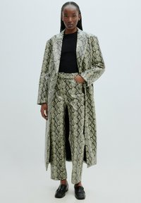 Jas en broekset met slangenleerpatroon in groen en zwart, met een lange snit, een gladde textuur en voorkristal. Zwarte shirt eronder.