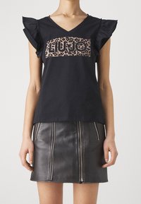 Camiseta de algodón negra con mangas acampanadas y un logotipo de leopardo "LIU JO" en el frente, combinada con una falda de cuero negra con cremallera.