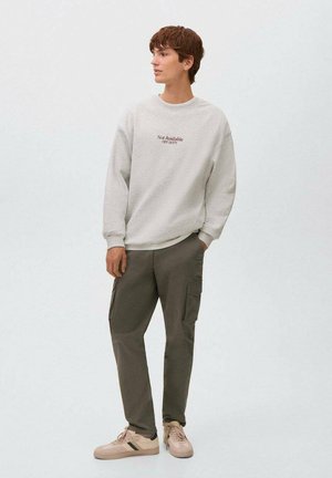 Lichtgrijze sweatshirt met tekstdetails, gecombineerd met olijfgroene cargobroeken met zakken. Beige sneakers met groene accenten maken de look af.