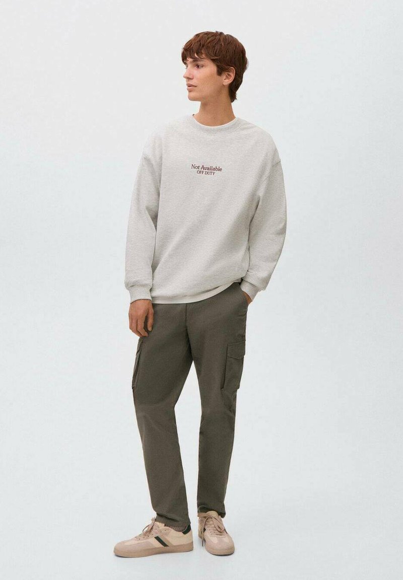 Ljusgrå sweatshirt med textdetalj, tillsammans med olivgröna cargobyxor med fickor. Beiga sneakers med gröna accenter fulländar looken.