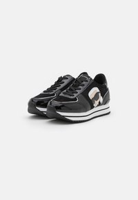 Zapatillas de charol negro con una franja blanca y un diseño de logo en el costado. Superficie texturizada con cordones en la parte frontal y cuello acolchado.