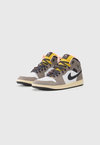 High-top sneakers featuring a beige and grey suede upper, white leather panels, black accents, vibrant yellow laces, and a textured black sole.